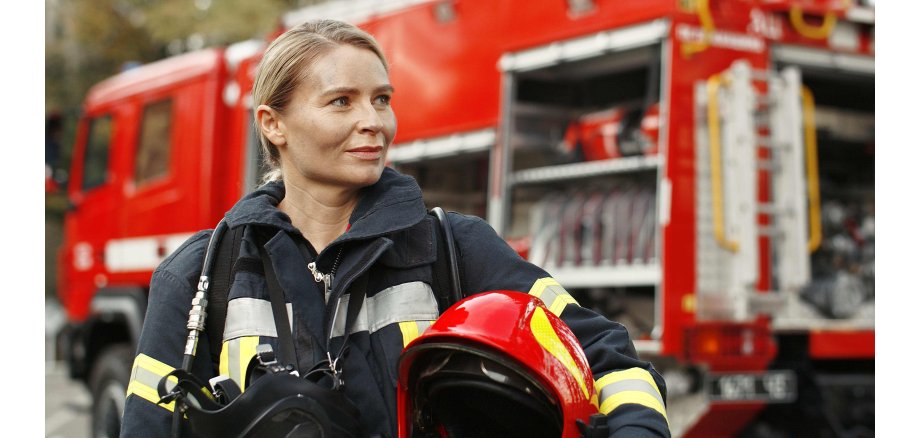 Portrait of young woman firefighter standing near fire truck.