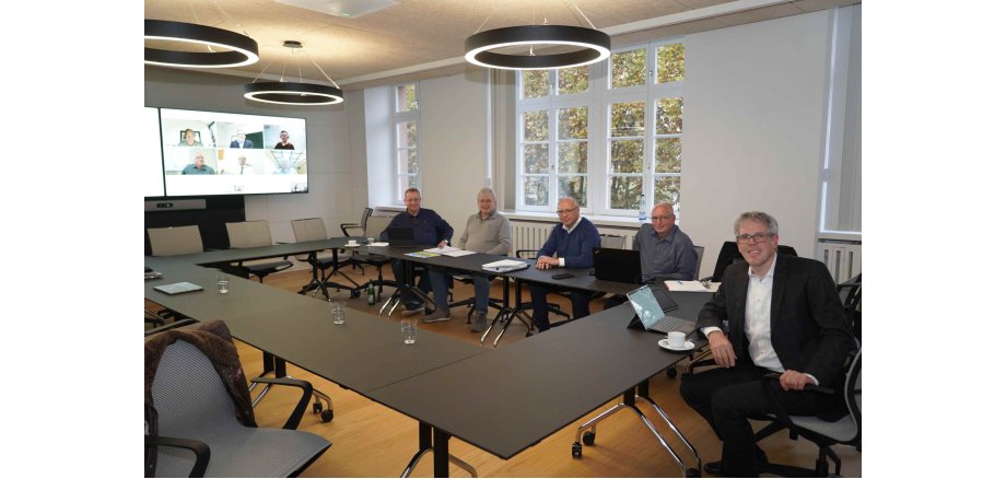 Landrat Engelhardt und Vertreter der Beteiligten bei der hybrid stattfindenden Gesellschafterversammlung am Tisch sitzend bzw. auf dem Monitor zu sehen.