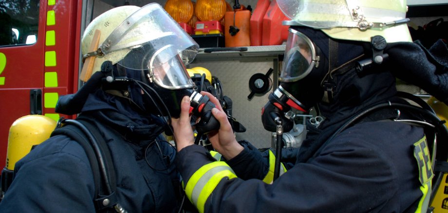 Auf dem Bild sind zwei Feuerwehrmänner mit Atemschutzgeräten zu sehen.