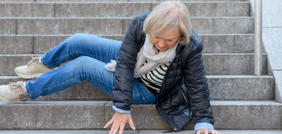 Eine ältere Frau stürzt im Außenbereich eine steinerne Treppe herunter.