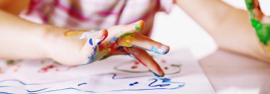 Nahaufnahme von einer Kinderhand, die mit Fingerfarben etwas auf ein weißes Blatt Papier malt.