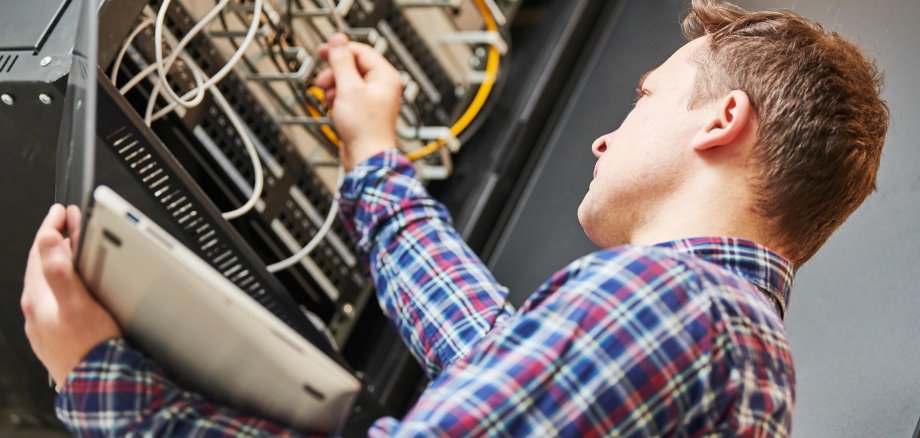 IT-Fachmann von schräg unten aufgenommen, nur von der Seite zu sehen, überprüft die Anschlüsse an einem Server.